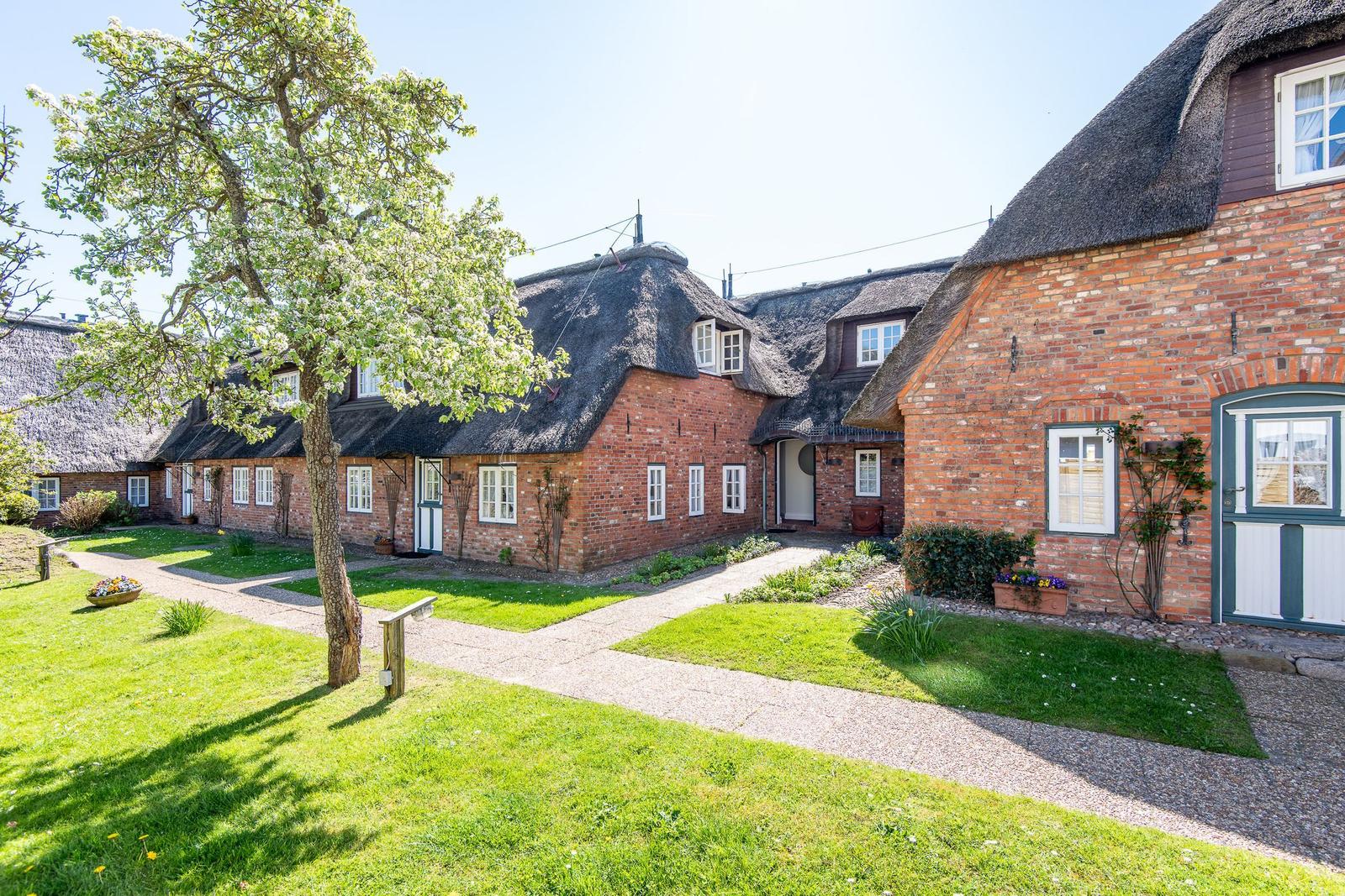Red brick house with thatched roof and green garden
