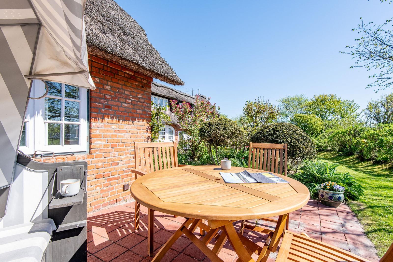 Terrace with wooden table and chairs in front of a house with thatched roof.