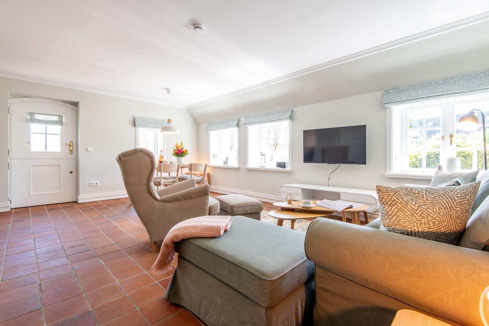 Living and dining area with sofa, armchair, and TV mounted on the wall.