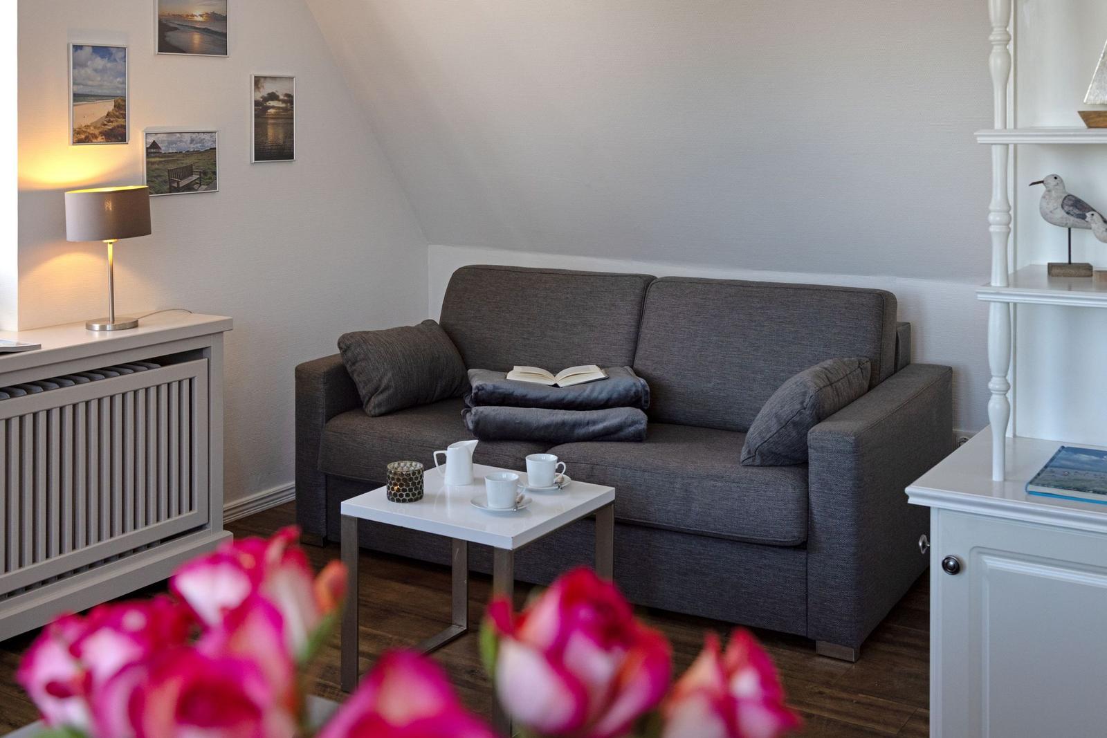 Ein Wohnzimmer mit grauem Sofa, weißem Tisch und Wandbildern.