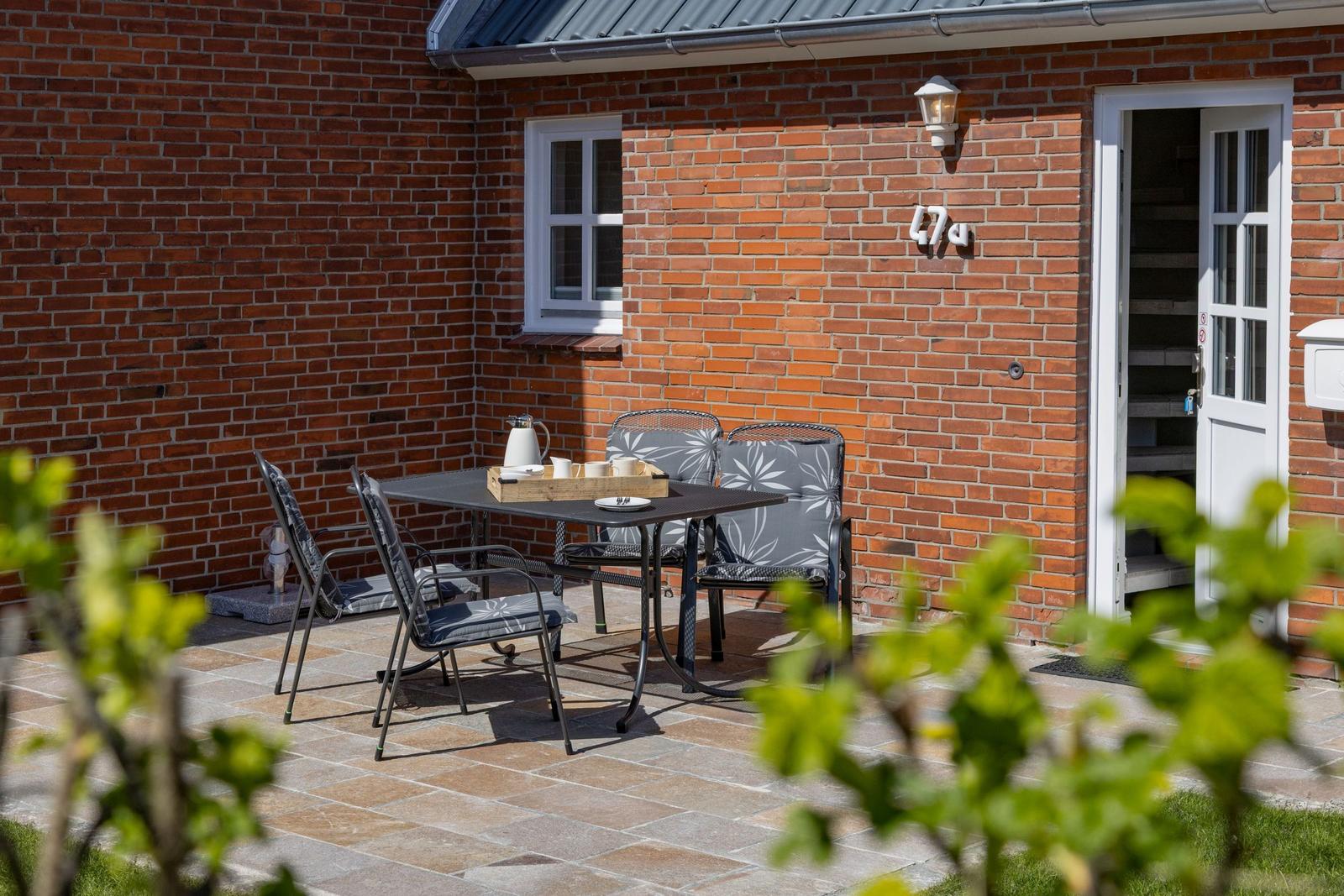 Terrasse mit Tisch und Stühlen vor rotem Backsteinhaus mit Eingangstür.