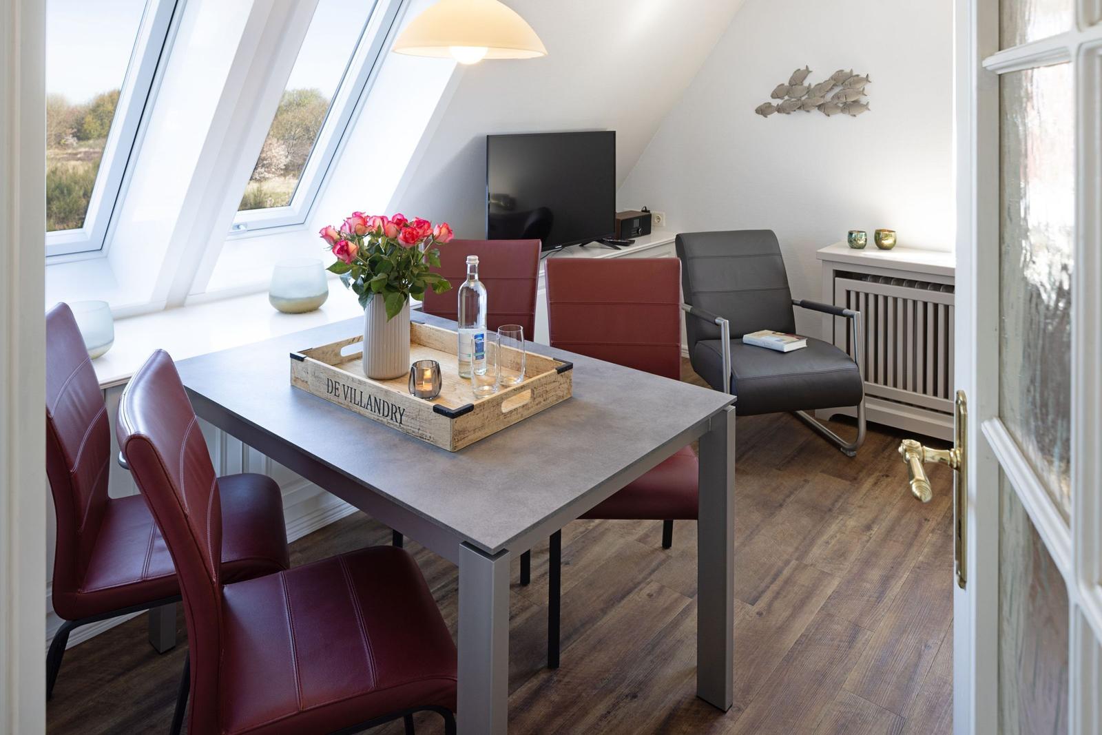 Essbereich mit Tisch, roten Stühlen und großen Dachfenstern. Fernseher und Sessel sind vorhanden.