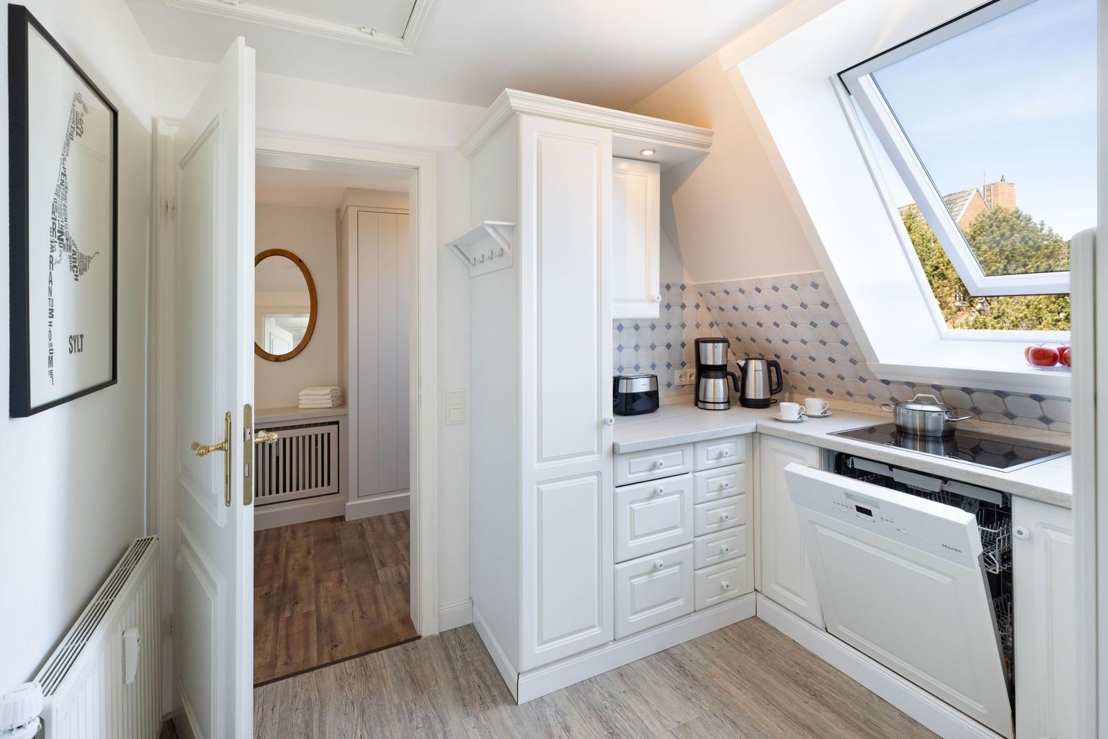 Küche mit weißen Schränken, Waschmaschine und Dachfenster. Tür führt in Schlafzimmer.