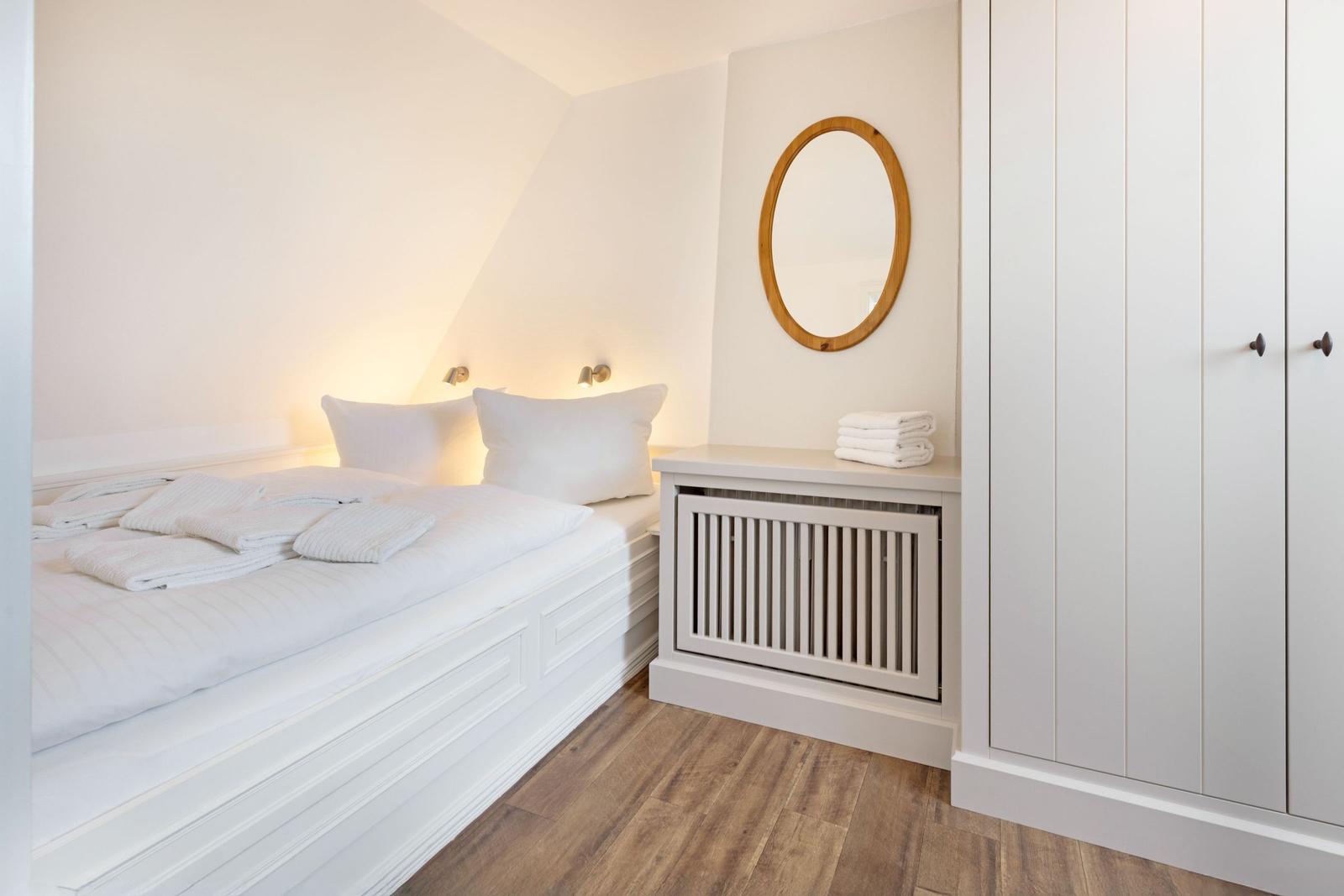 Schlafzimmer mit weißem Bett, Holzboden und runden Spiegel.
