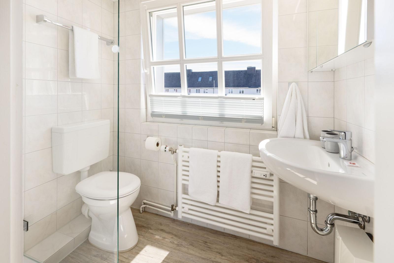 Badezimmer mit Toilette, Waschbecken und Fenster mit Blick auf Dächer.