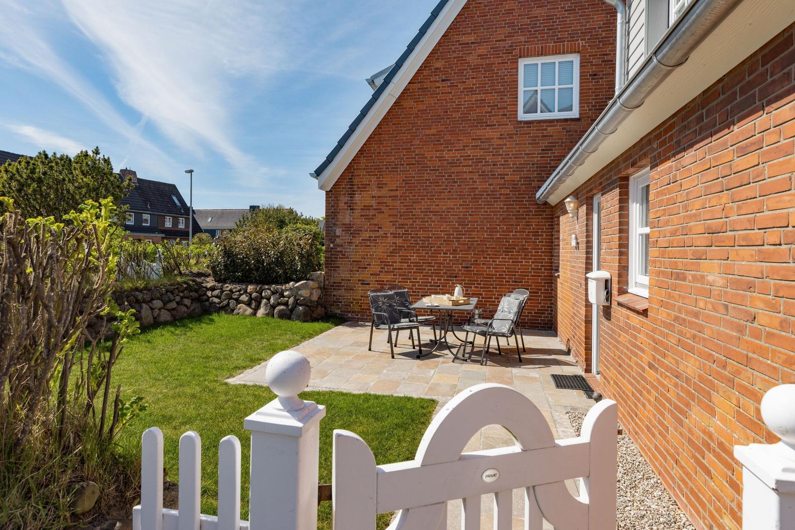 Roter Backsteinbau mit Terrasse, Garten und Gartenzaun.