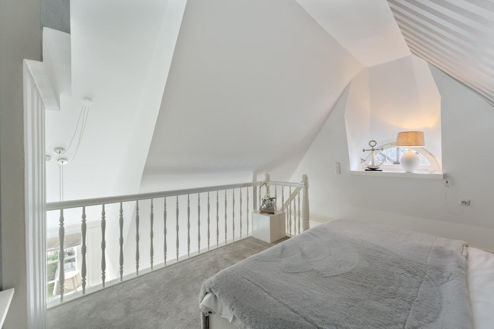Schlafzimmer mit Dachschrägen, weißer Balustrade und Bett unter Fenster