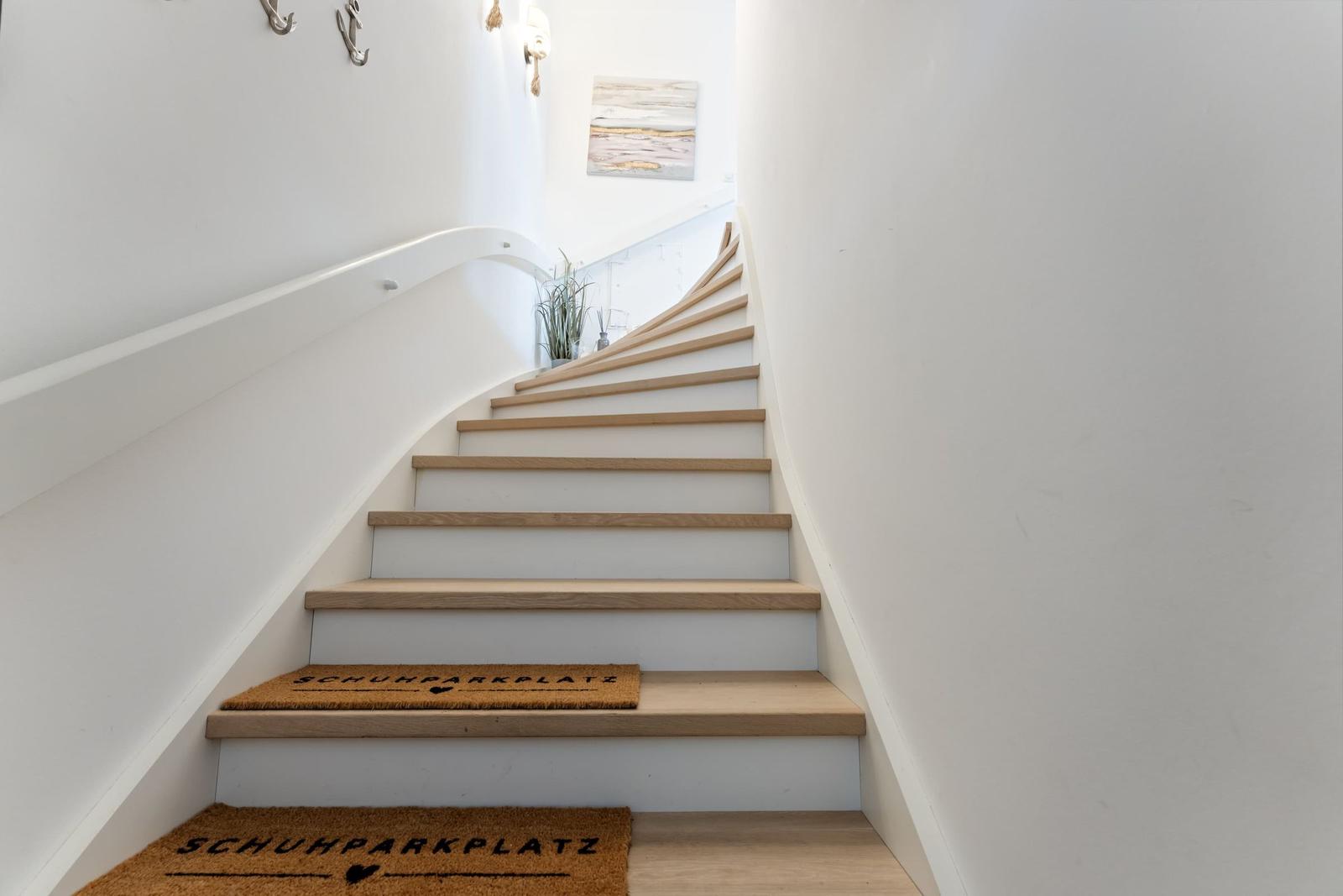 Eine Treppe mit Holzstufen und weißen Wänden. An der Wand hängt ein Bild.