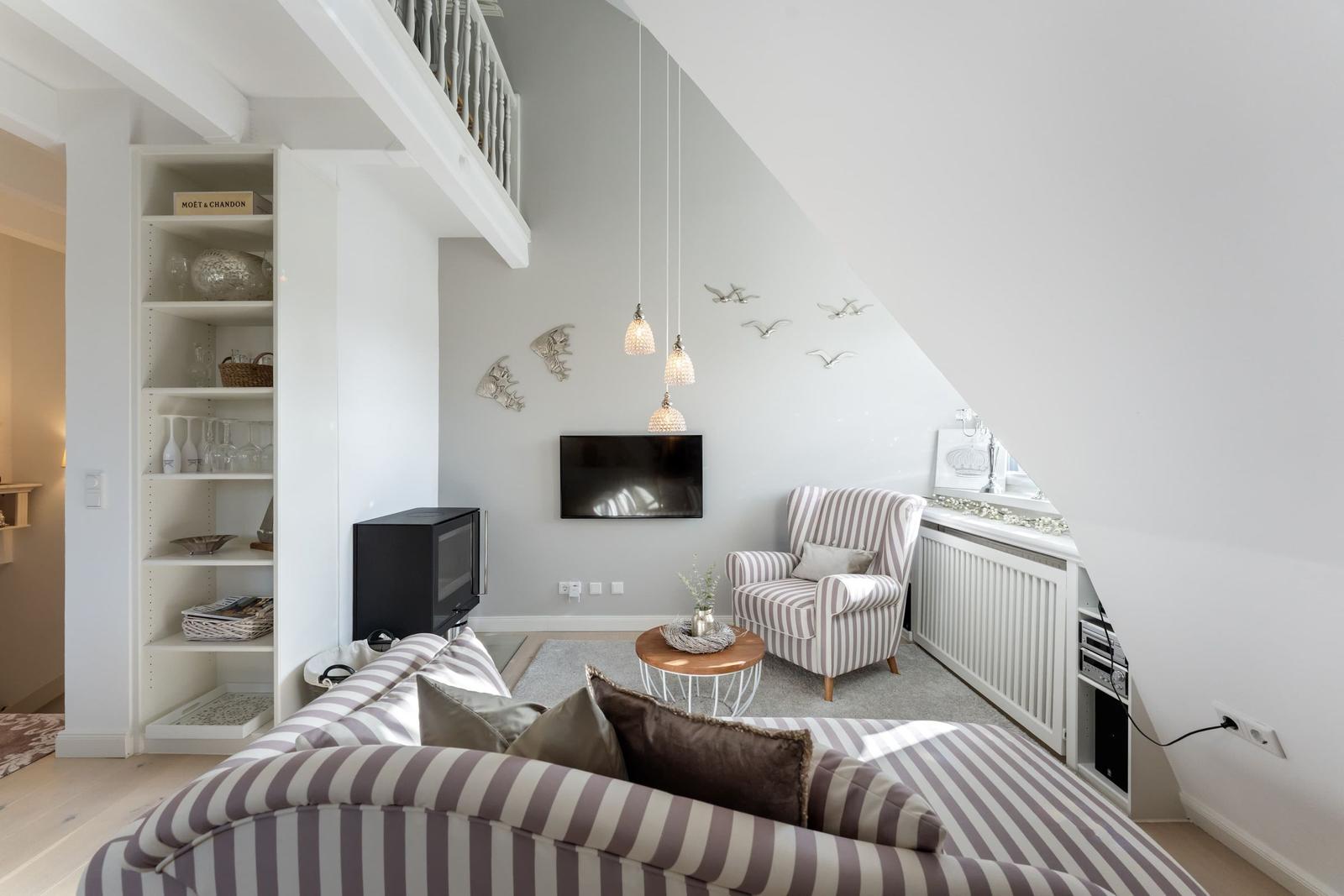 Wohnzimmer mit Sofa, Sessel und Fernseher unter Dachschräge.