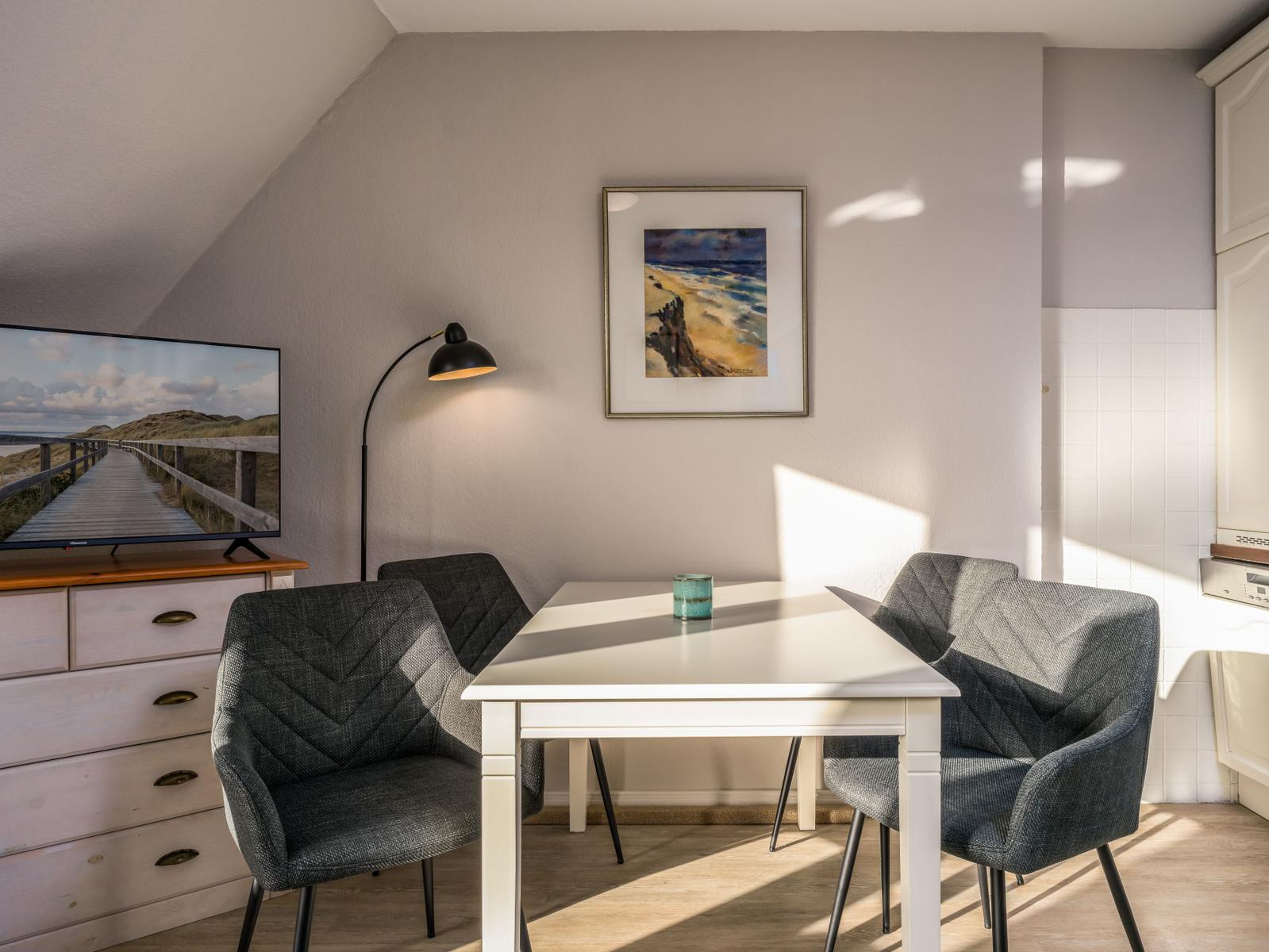 Esszimmer mit weißem Tisch, vier Stühlen und Fernseher an der Wand.