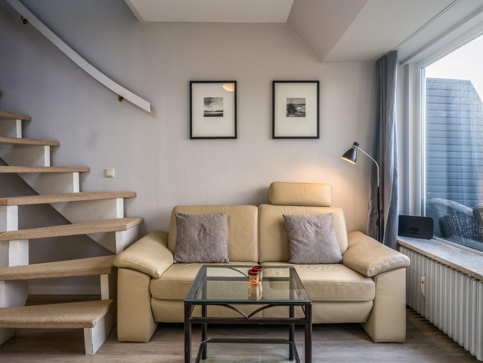 Ein Wohnzimmer mit einem Sofa, einem Glas-Tisch und einer Treppe.
