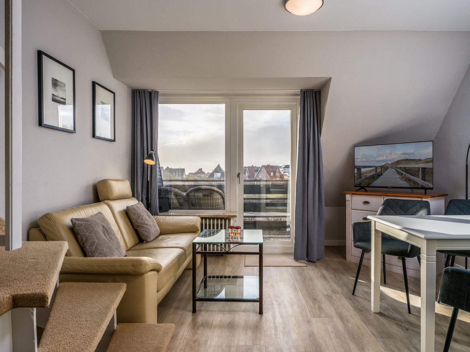 Wohnzimmer mit Sofa, Esstisch und TV. Balkon mit Blick auf Dächer.