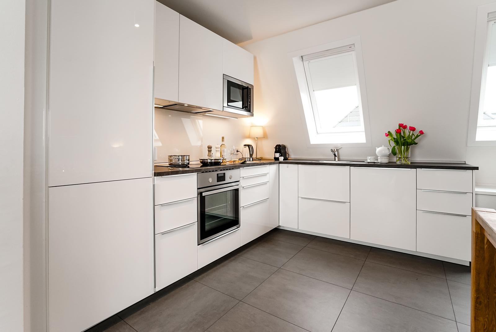 Moderne Küche mit weißen Schränken, Edelstahlgeräten und dunklem Arbeitsplatz.