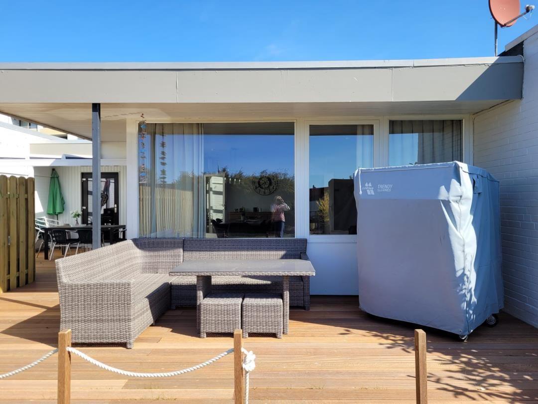Terrace with seating group, table, and covered grill. Background: windows and house wall.
