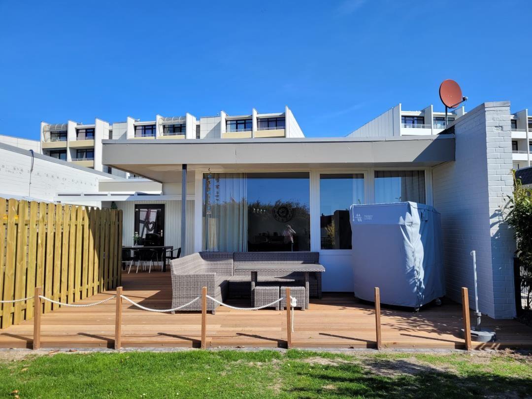 Deck with seating area and grill, adjacent lawn and modern building in background.