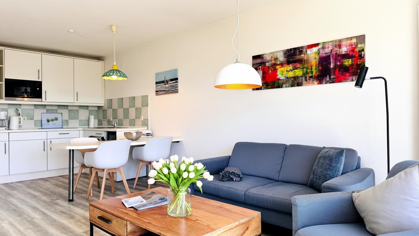 Wohn- und Essbereich mit Küchenzeile, Sofa und Blumen.