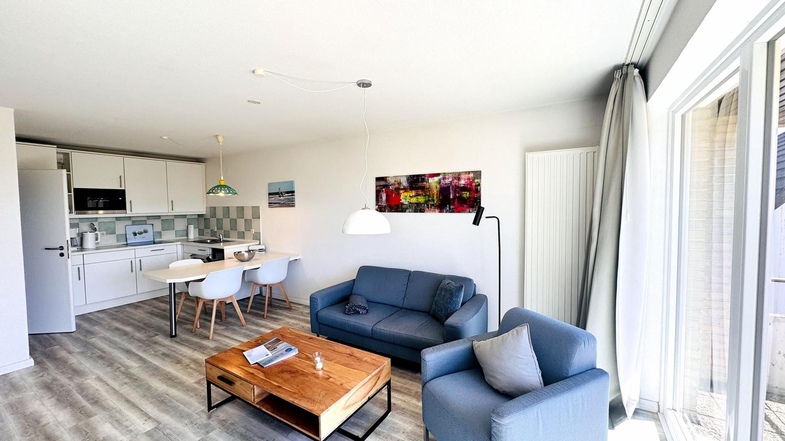 Wohnung mit Küche, Essbereich und Wohnzimmer mit blauer Couch und Holztisch.