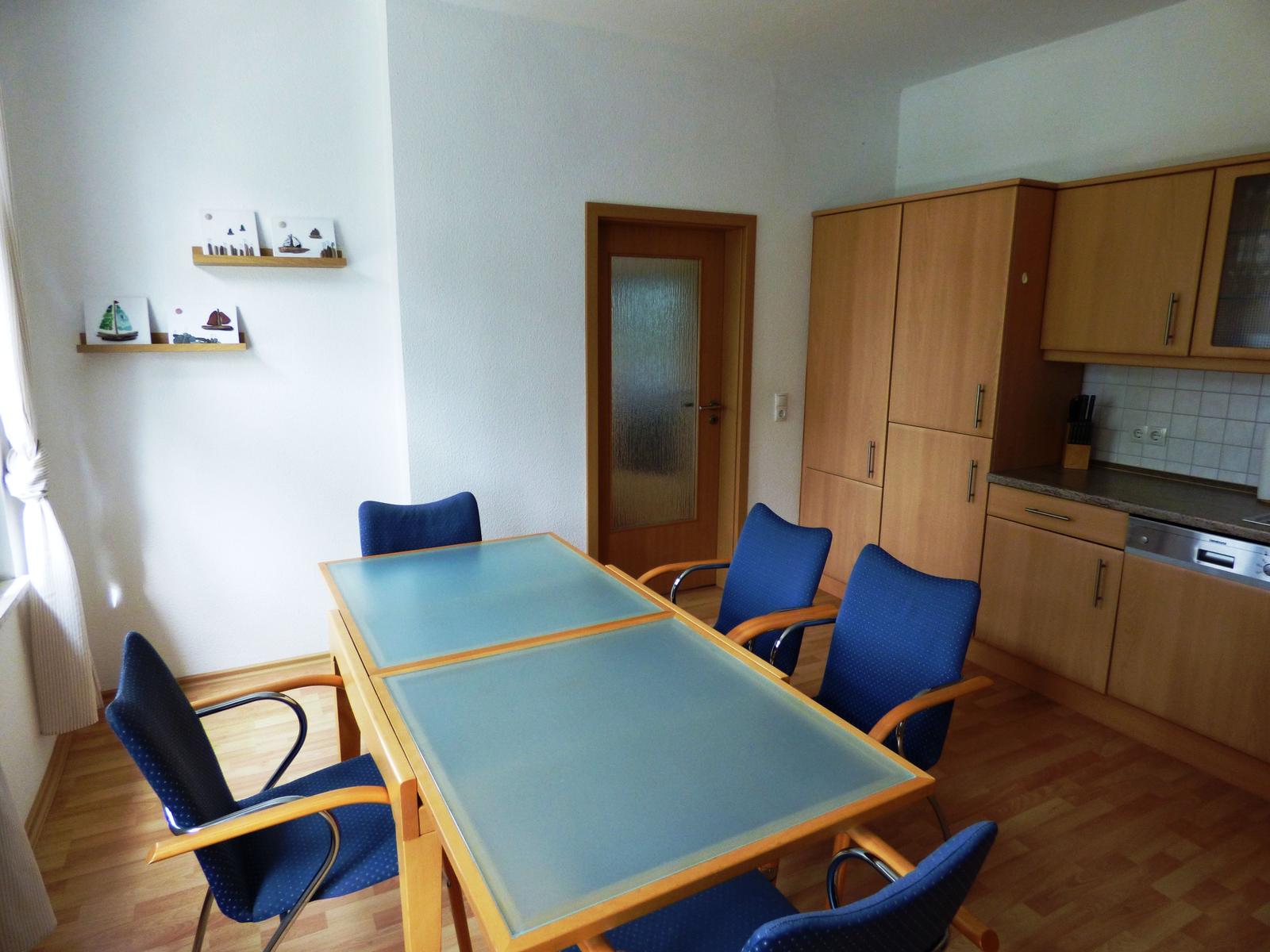 Essbereich mit Tisch und Stühlen, Küchenzeile und Schränke im Hintergrund.