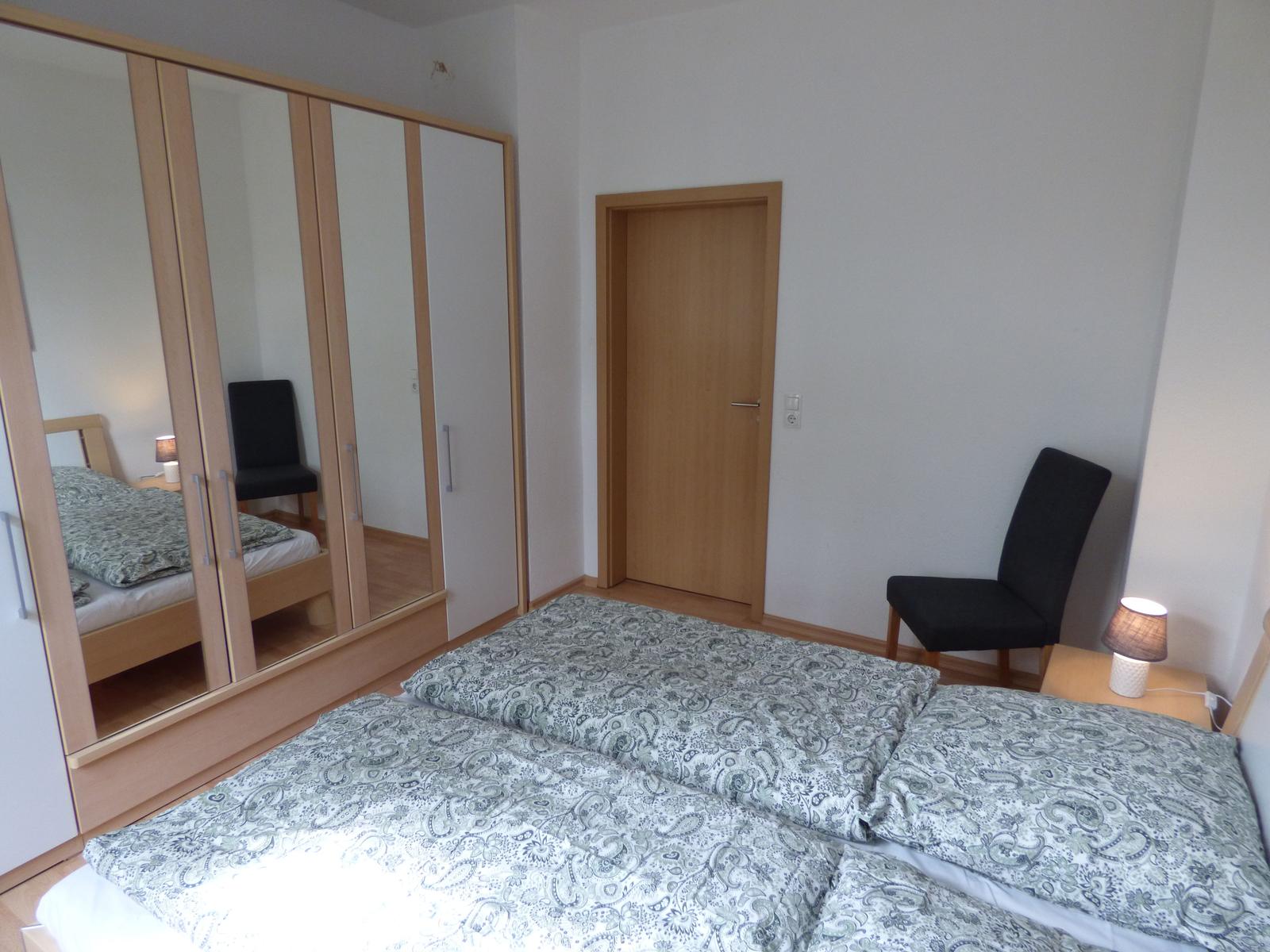 Schlafzimmer mit Doppelbett, Spiegelschrank und Stuhl neben Nachttisch.