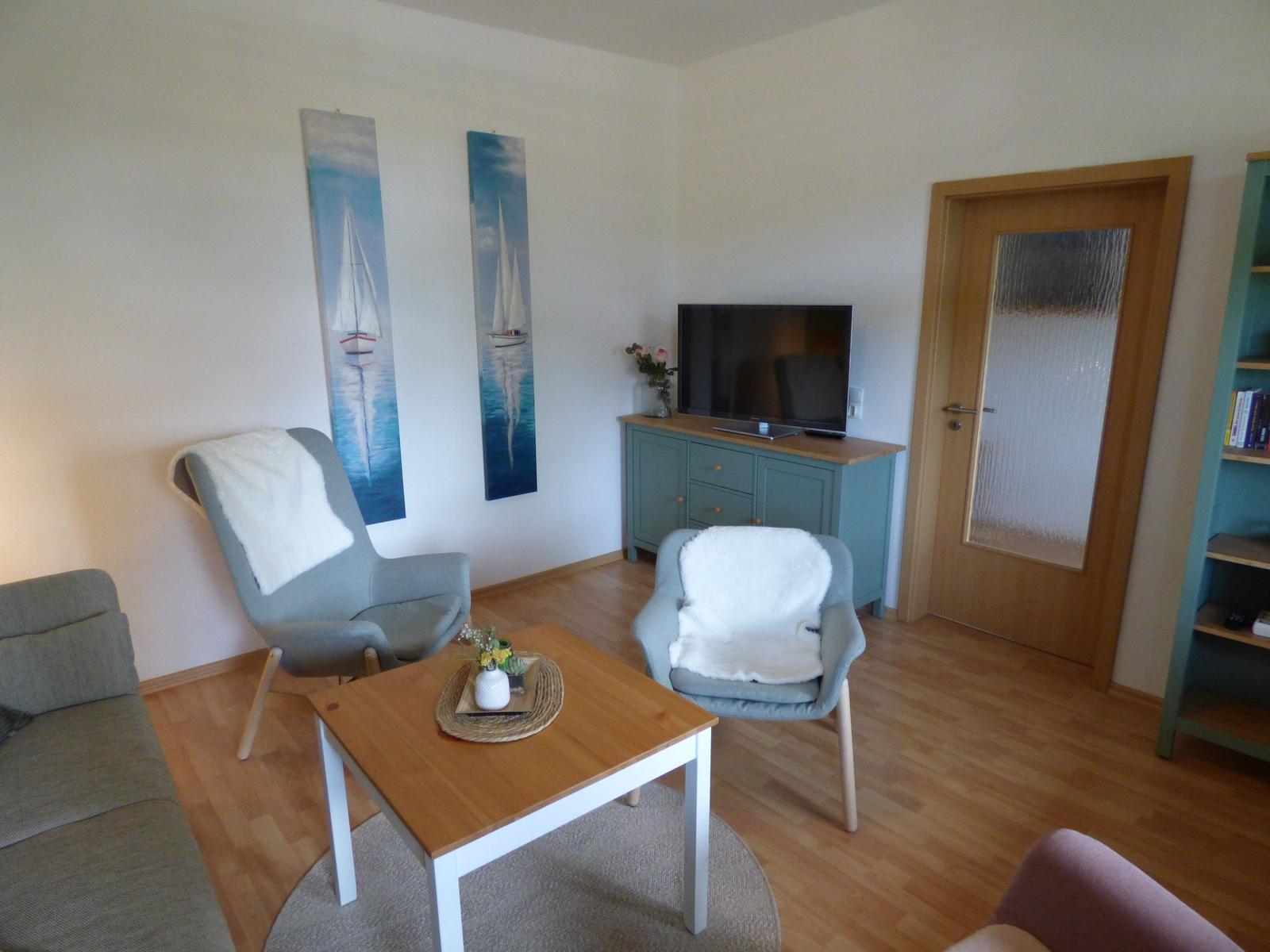 Wohnzimmer mit Sofa, zwei Stühlen, Fernseher und Holzboden.
