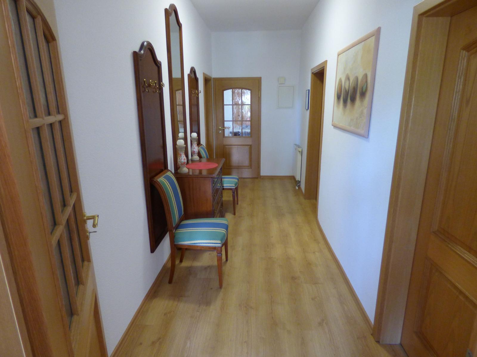 Flur mit Holzboden, Spiegel, Stuhl und Bild an der Wand.