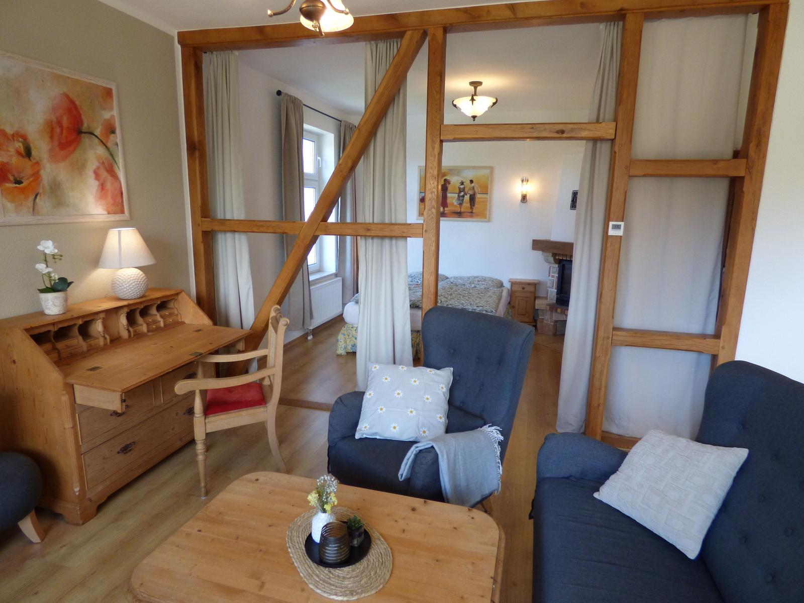 Wohnzimmer mit Holzrahmen, Sofa und Schreibtisch. Blick in Schlafzimmer mit Bett und Kamin.