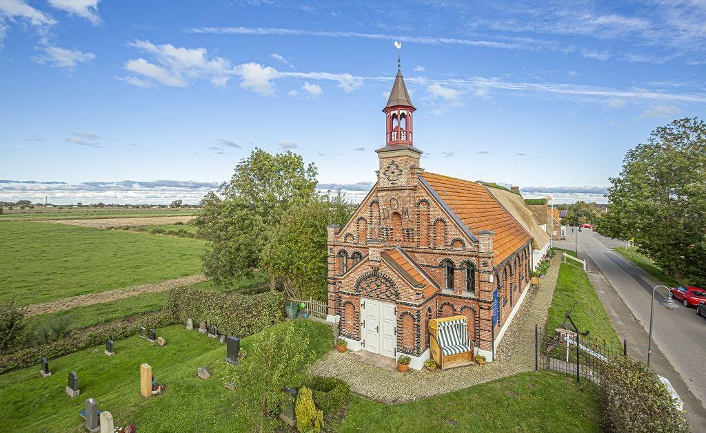 Historische Backstein-Kirche mit Turm und Friedhof, umgeben von grünen Wiesen und Bäumen.