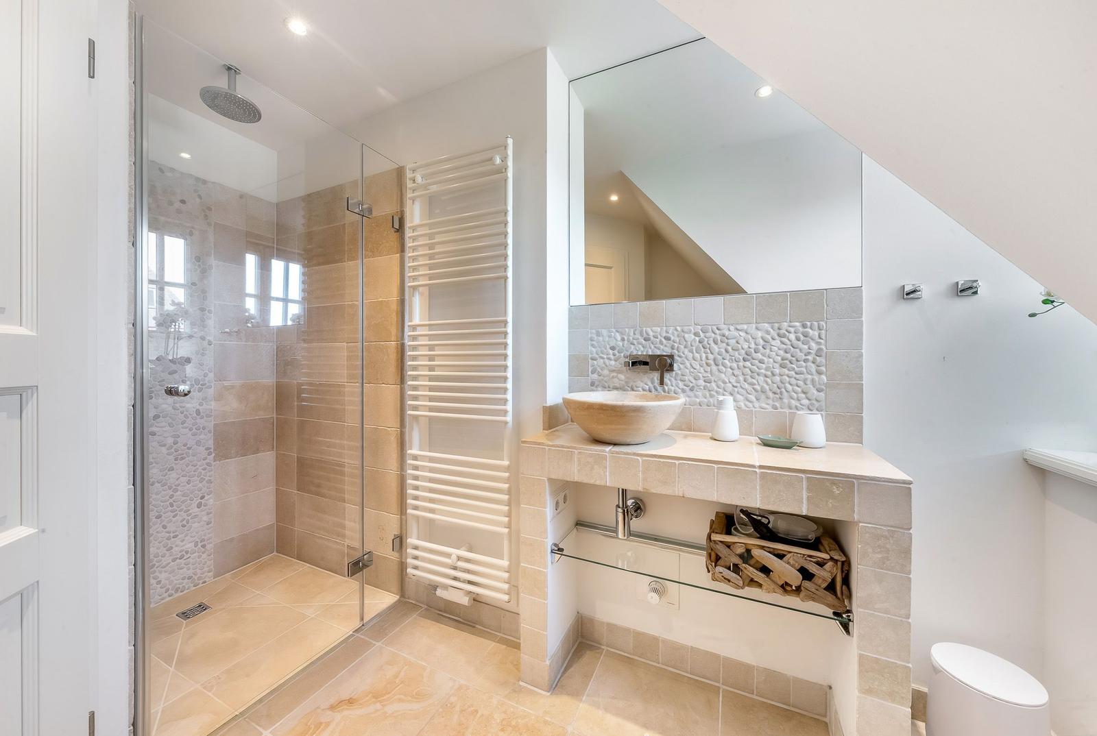 Dusche mit Glaswand, Waschbecken mit Spiegel und Heizkörper an der Wand.