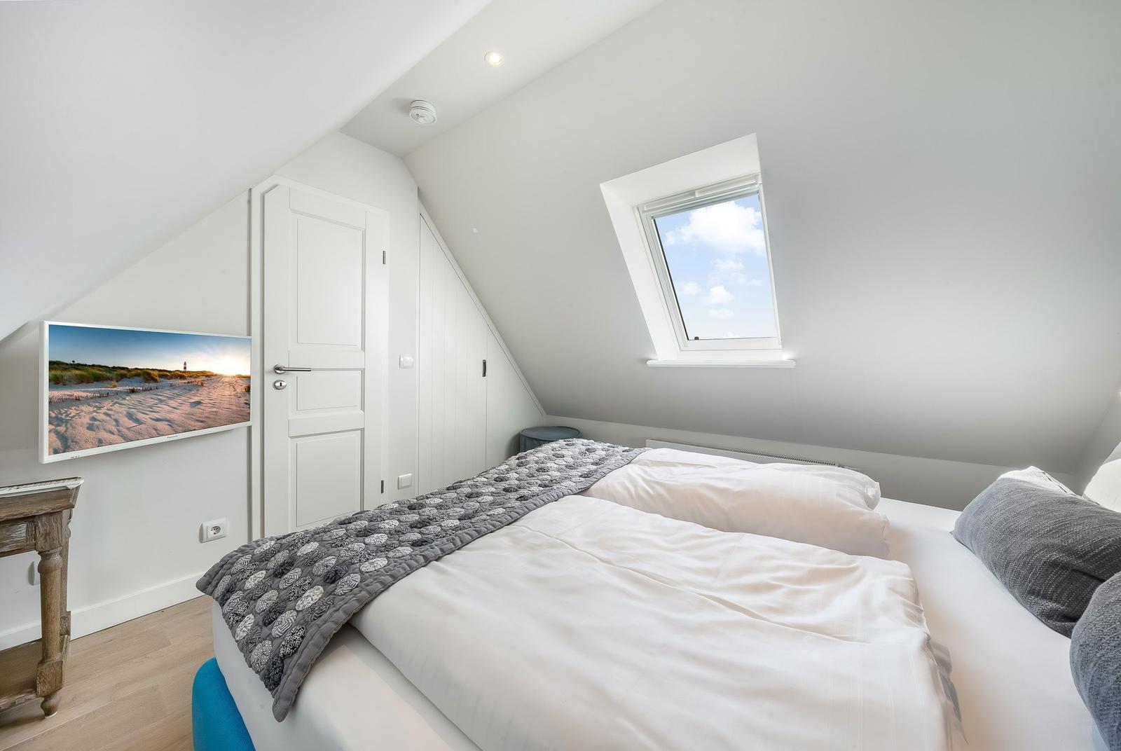 Schlafzimmer mit Dachfenster, Bett und Wandbild. Holztisch und weiße Türen.