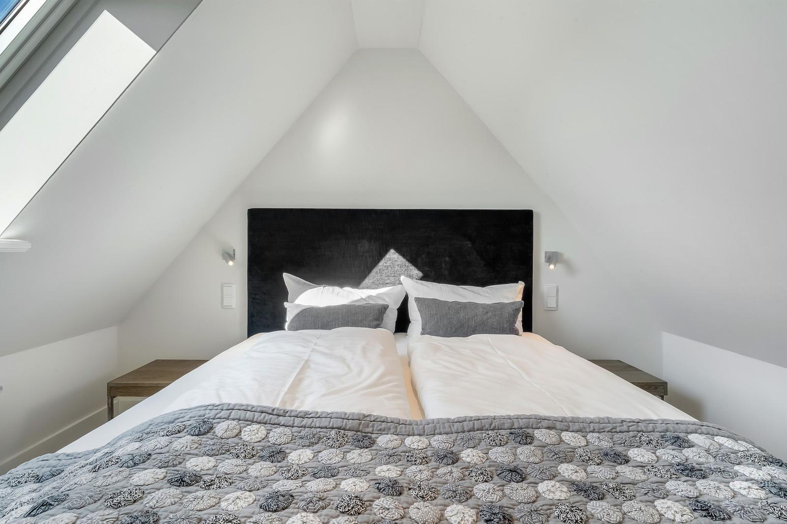 Schlafzimmer mit Dachschrägen, Doppelbett und Dachfenster.