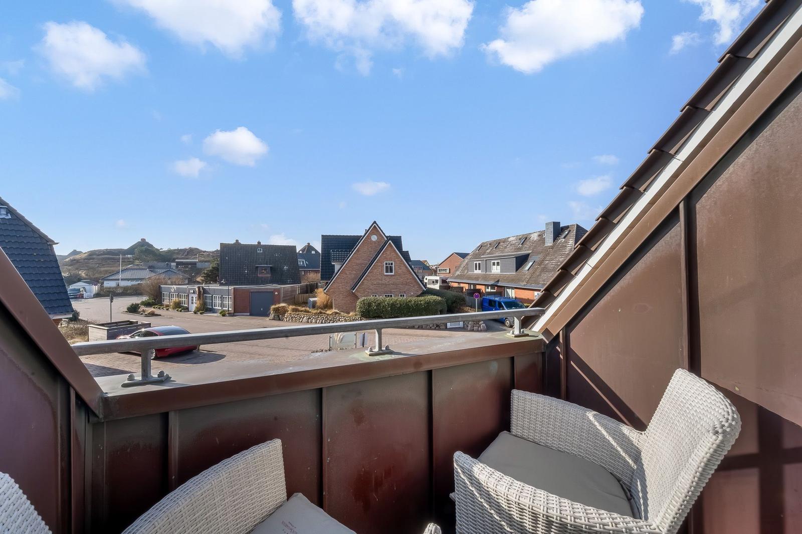 Balcony with two chairs overlooking houses and a clear blue sky.