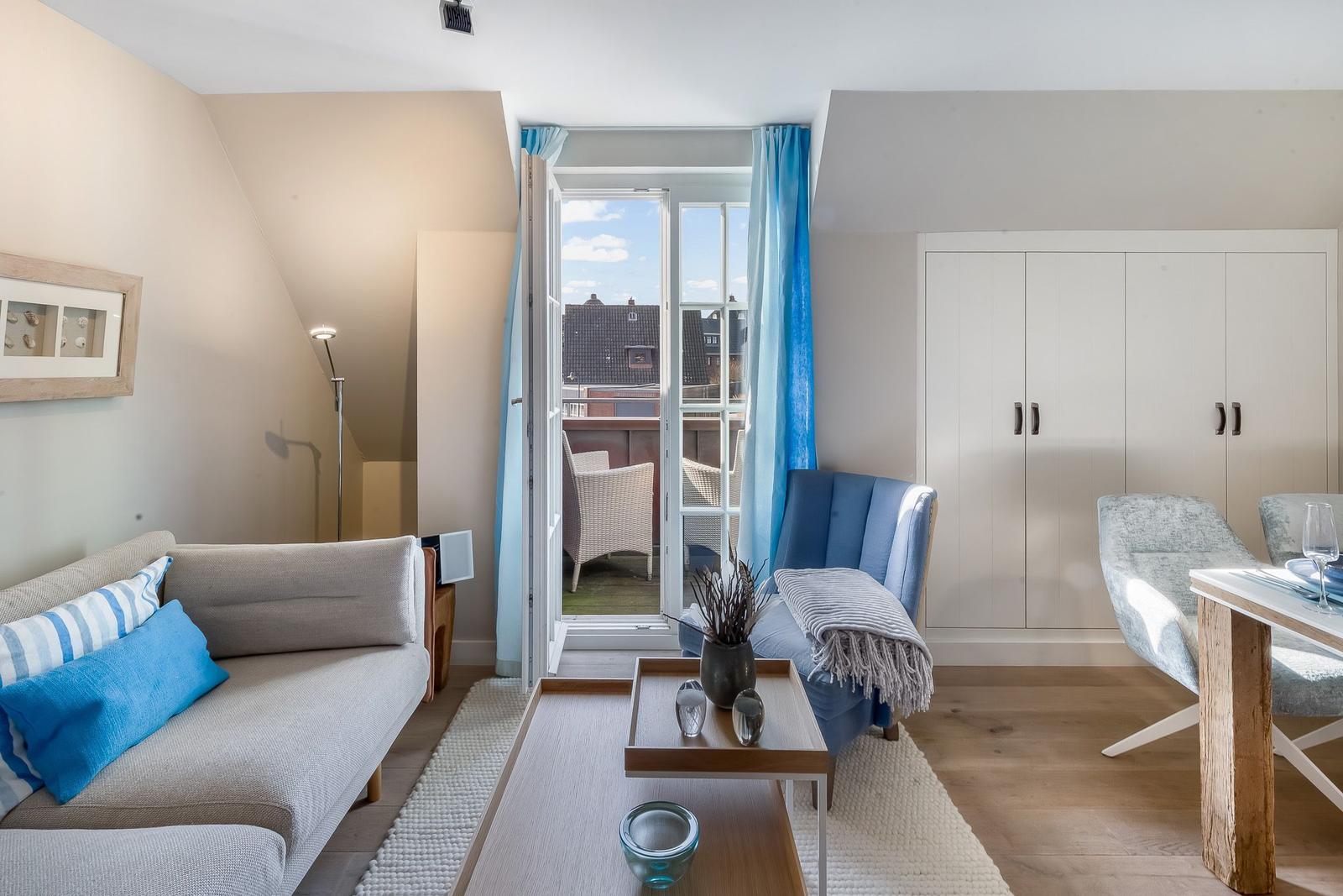 Wohnzimmer mit Sofa, Sessel und Terrasse. Hölzerner Boden und helle Wände.