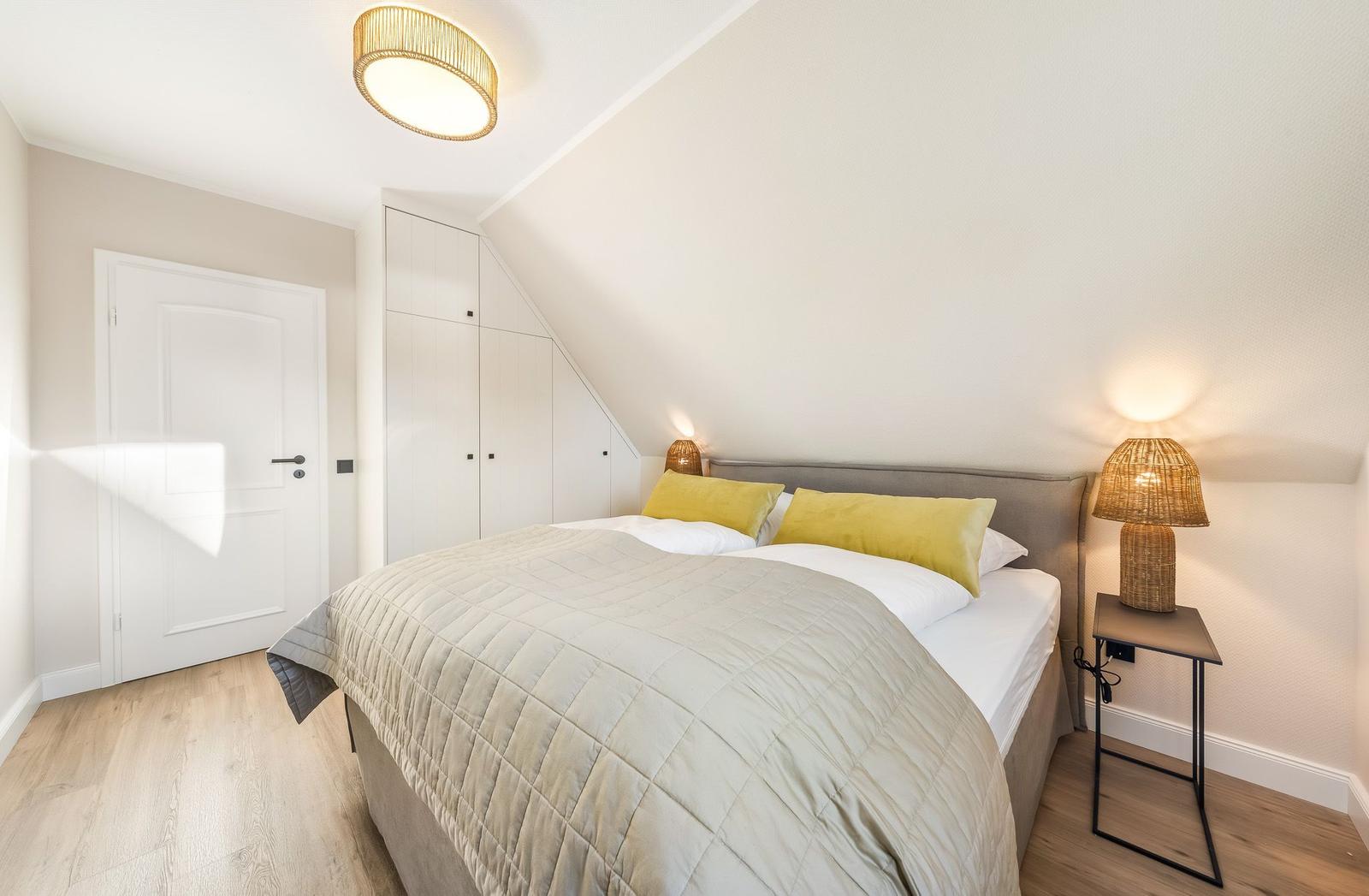 Schlafzimmer mit Dachschrägen, Bett mit Kissen, Nachttisch und Lampe.