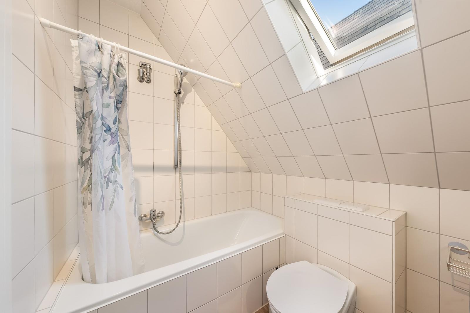 Badezimmer mit Dusche, Toilette und Dachfenster. Fliesenwand und Badewanne.