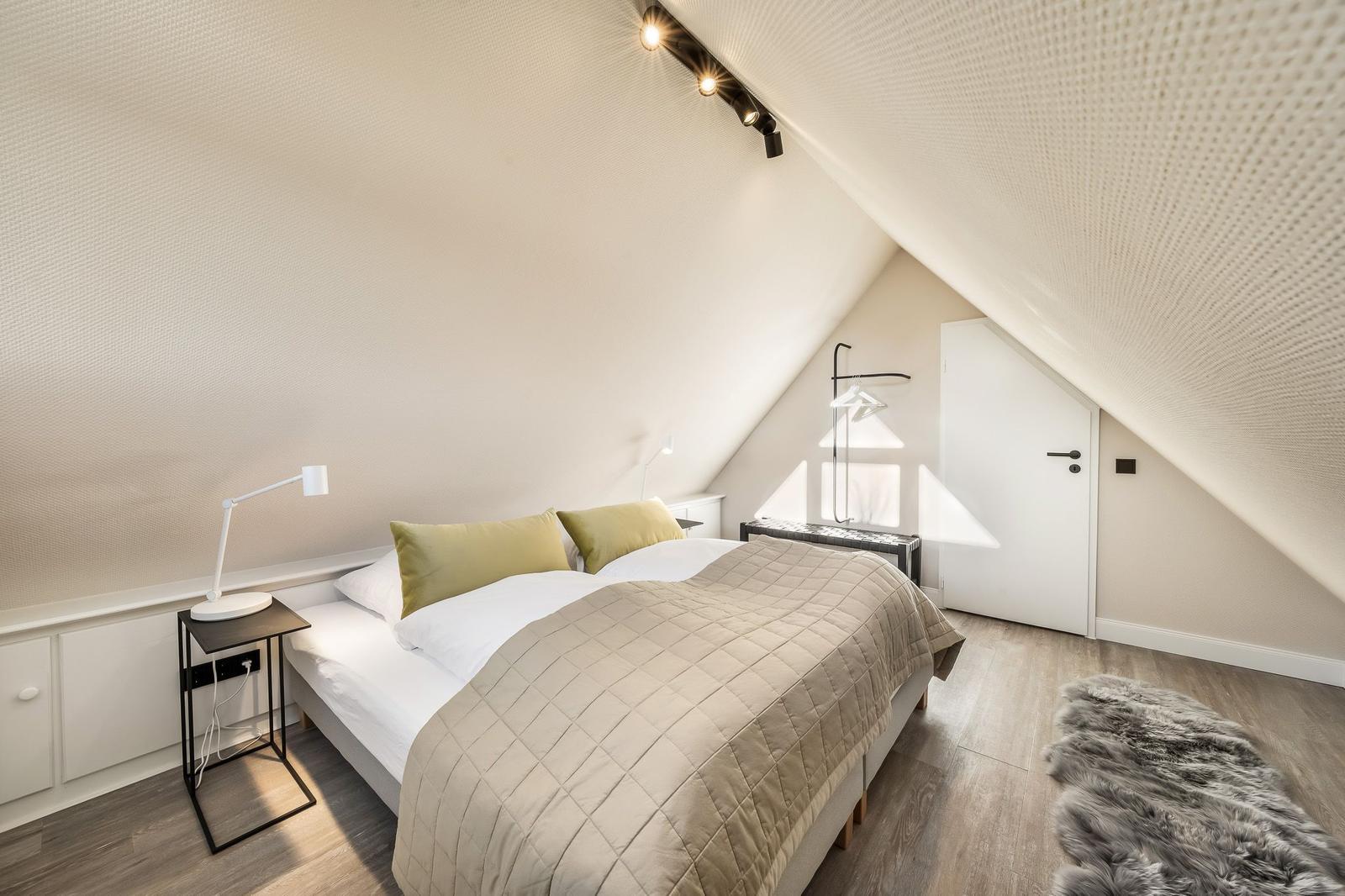 Schlafzimmer mit Dachschrägen, Bett, Nachttisch und Fellteppich.