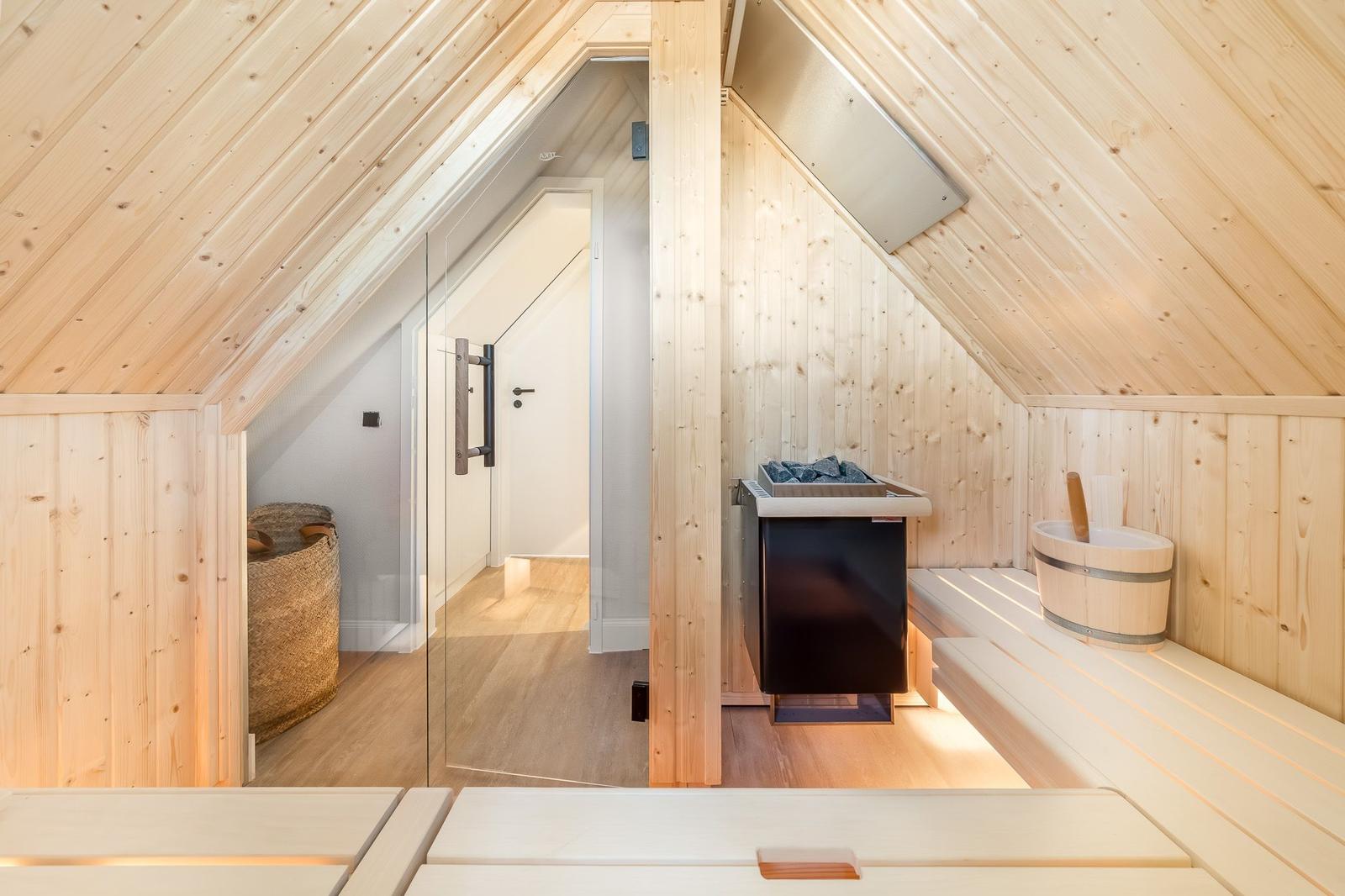 Sauna mit Holzverkleidung, Sitzbänken und Heizung. Glaswand trennt den Raum.