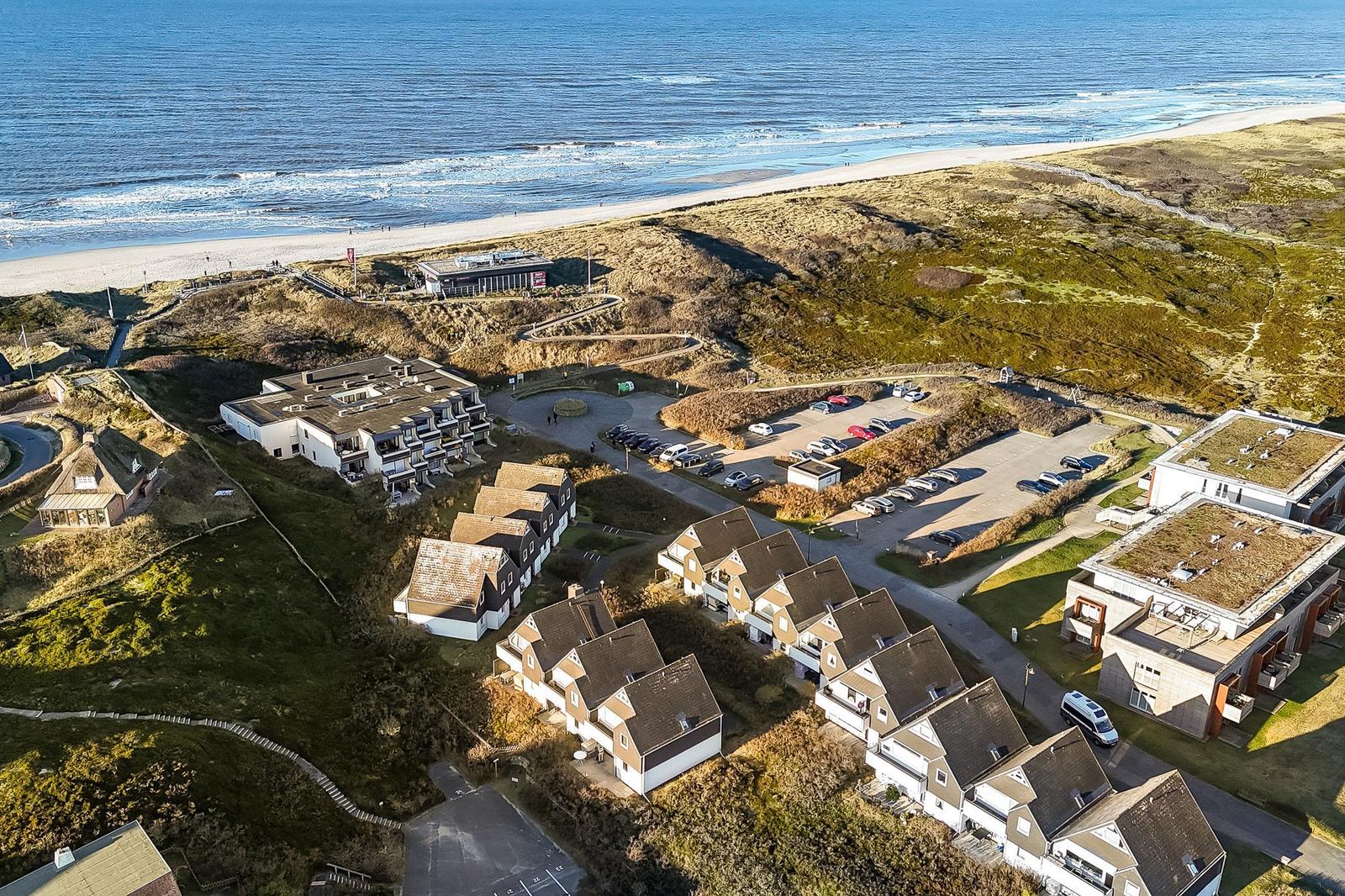 Strandnahe Ferienhäuser mit Parkplatz und Dünenlandschaft.