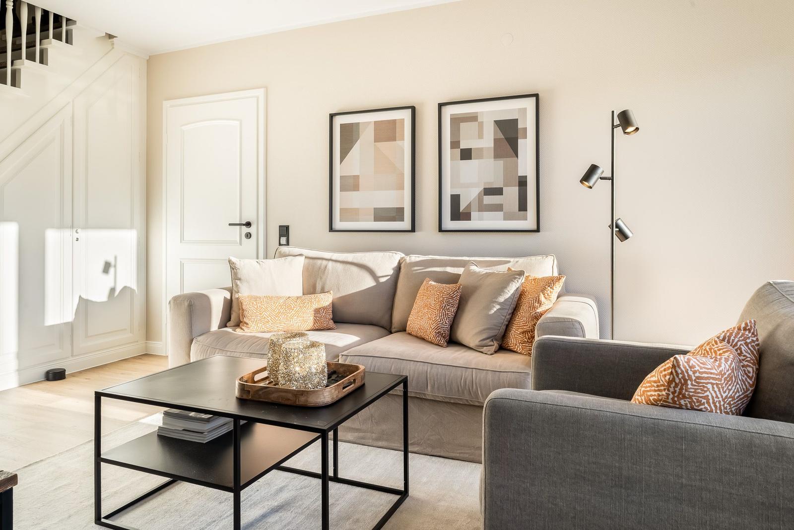 Wohnzimmer mit Sofa, Sessel, Tisch und Wandbildern.