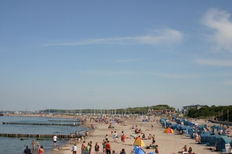 Strand mit vielen Besuchern, Sonnenschirmen und Booten im Hintergrund.