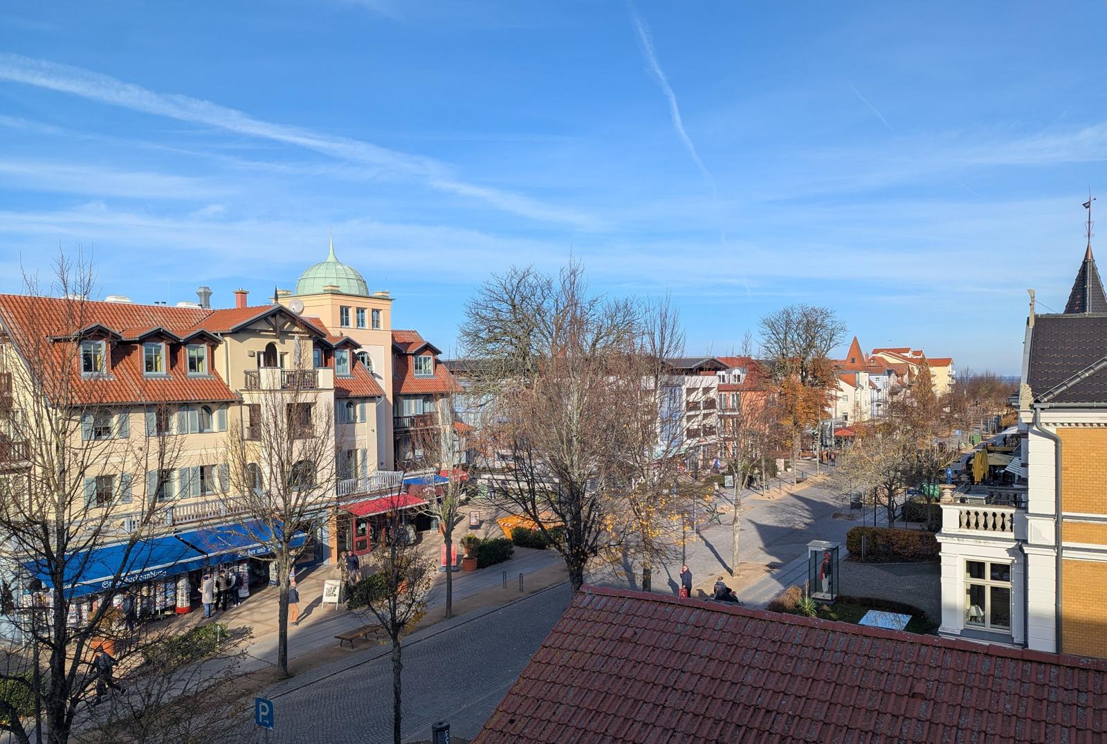 Panoramaansicht über einen Platz mit Gebäuden und Bäumen unter blauem Himmel.