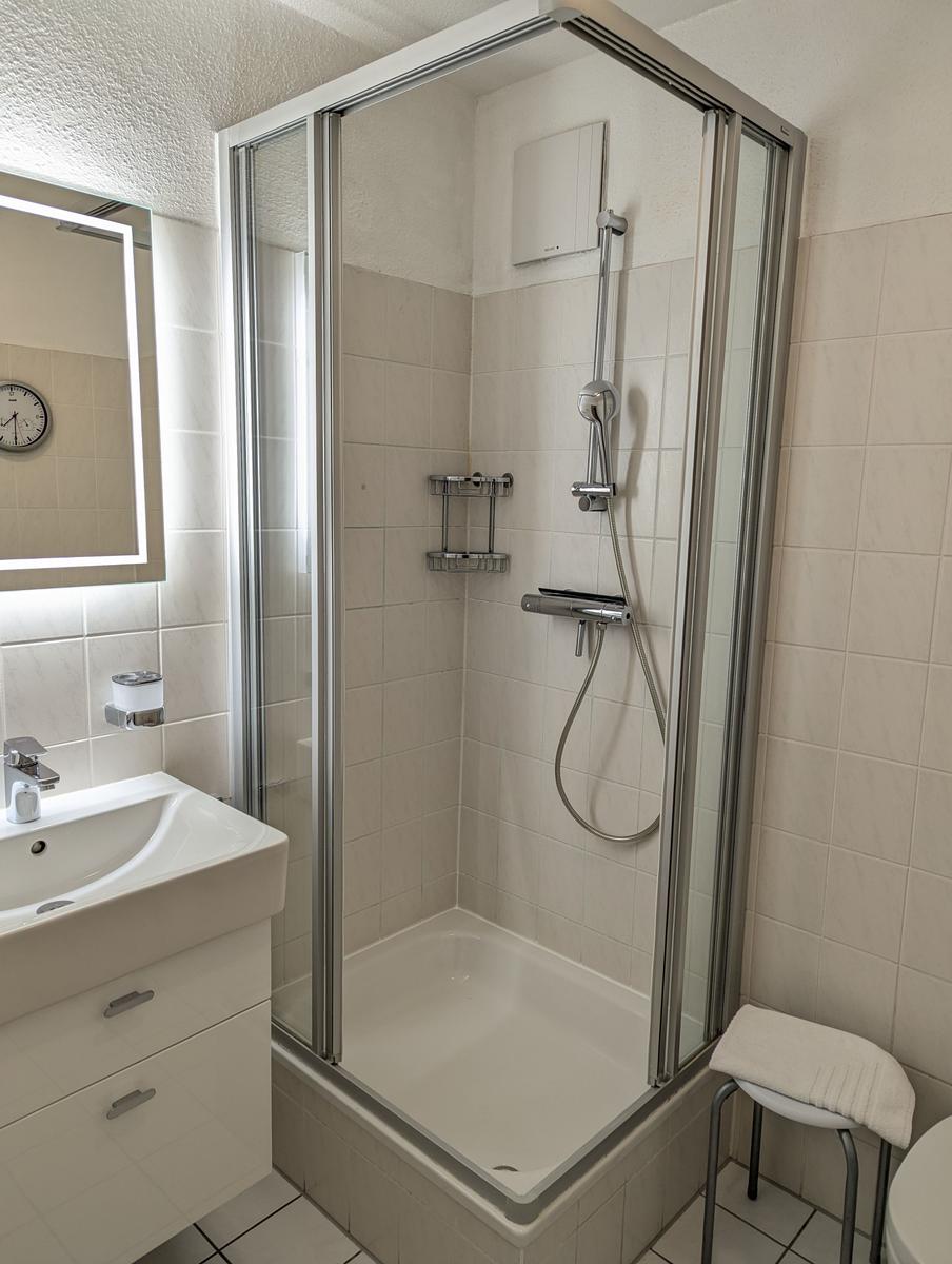 Badezimmer mit Dusche, Waschbecken und Spiegel.
