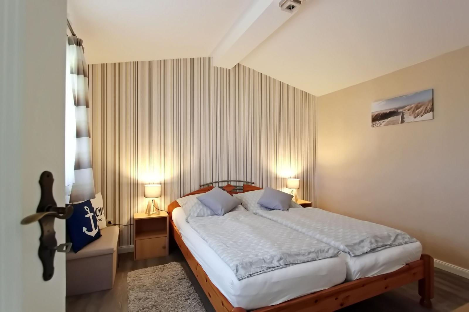 Schlafzimmer mit Doppelbett, Nachttischen und Streifenwand