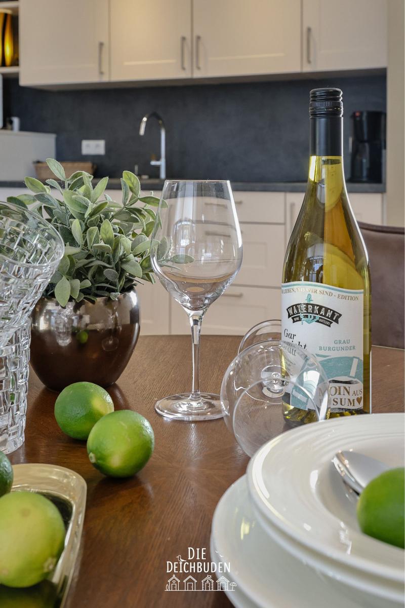 Tisch mit Weinglas, Flasche, Zitrusfrüchten und Pflanze in Küche.