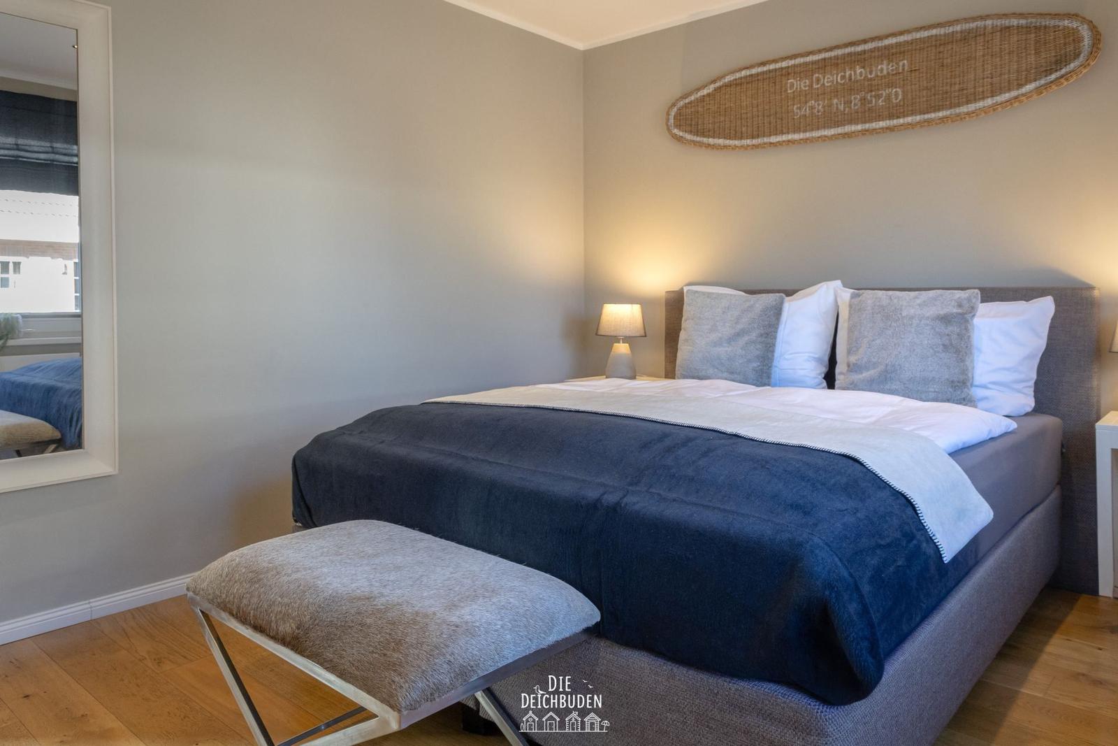 Schlafzimmer mit Bett, Kissen, Nachttisch und Wanddekoration.