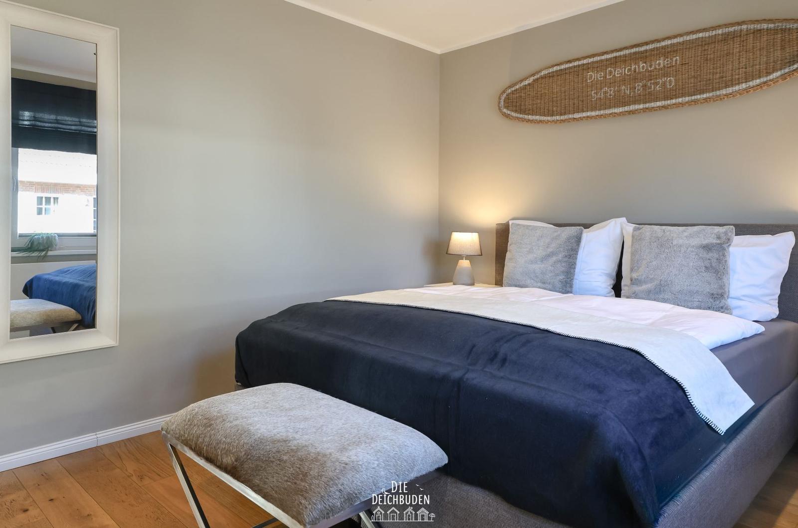 Schlafzimmer mit Bett, Spiegel und Wanddekoration.