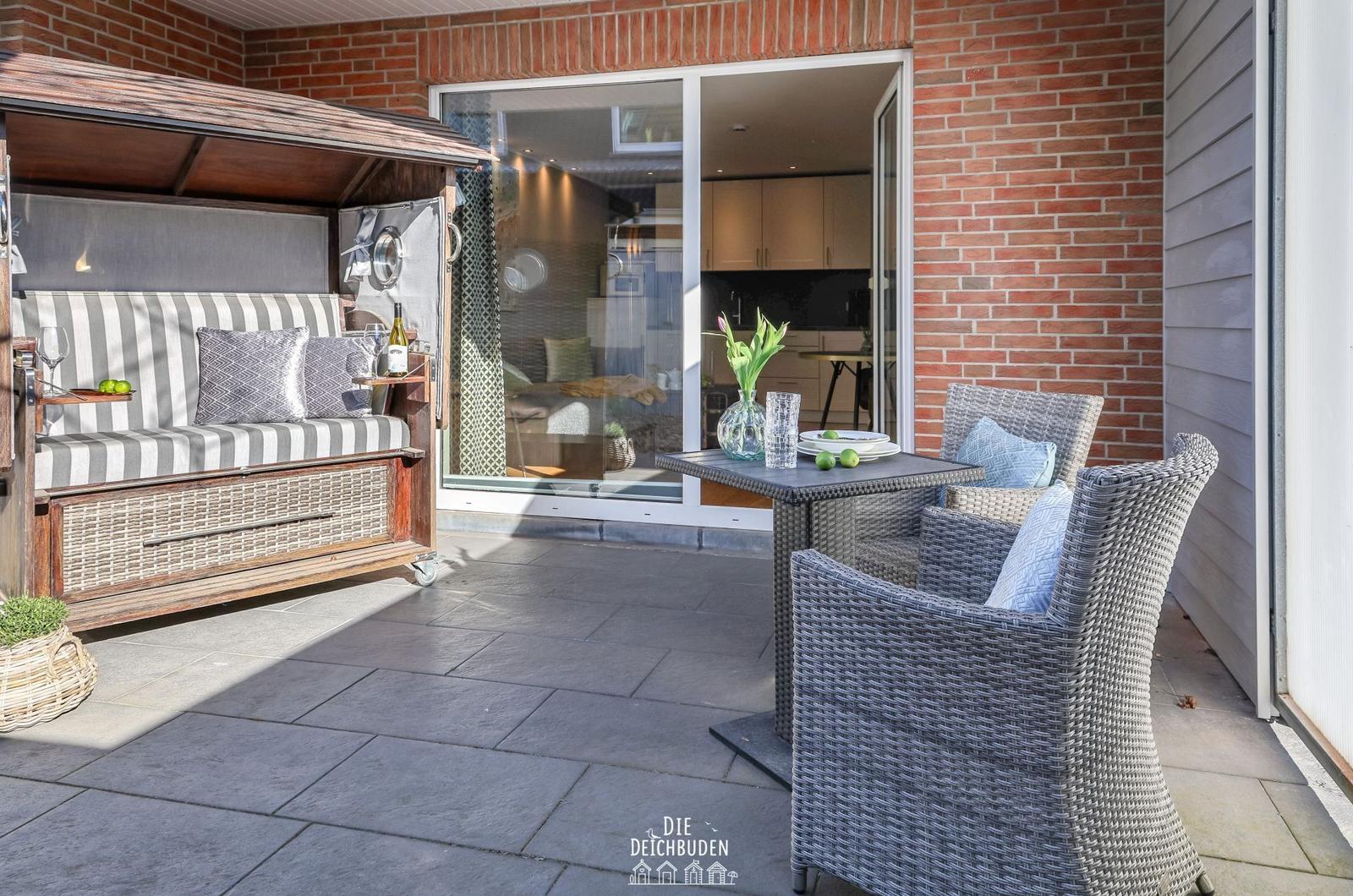 Terrasse mit Rattanmöbeln, Holzliege und Blick ins Innere.