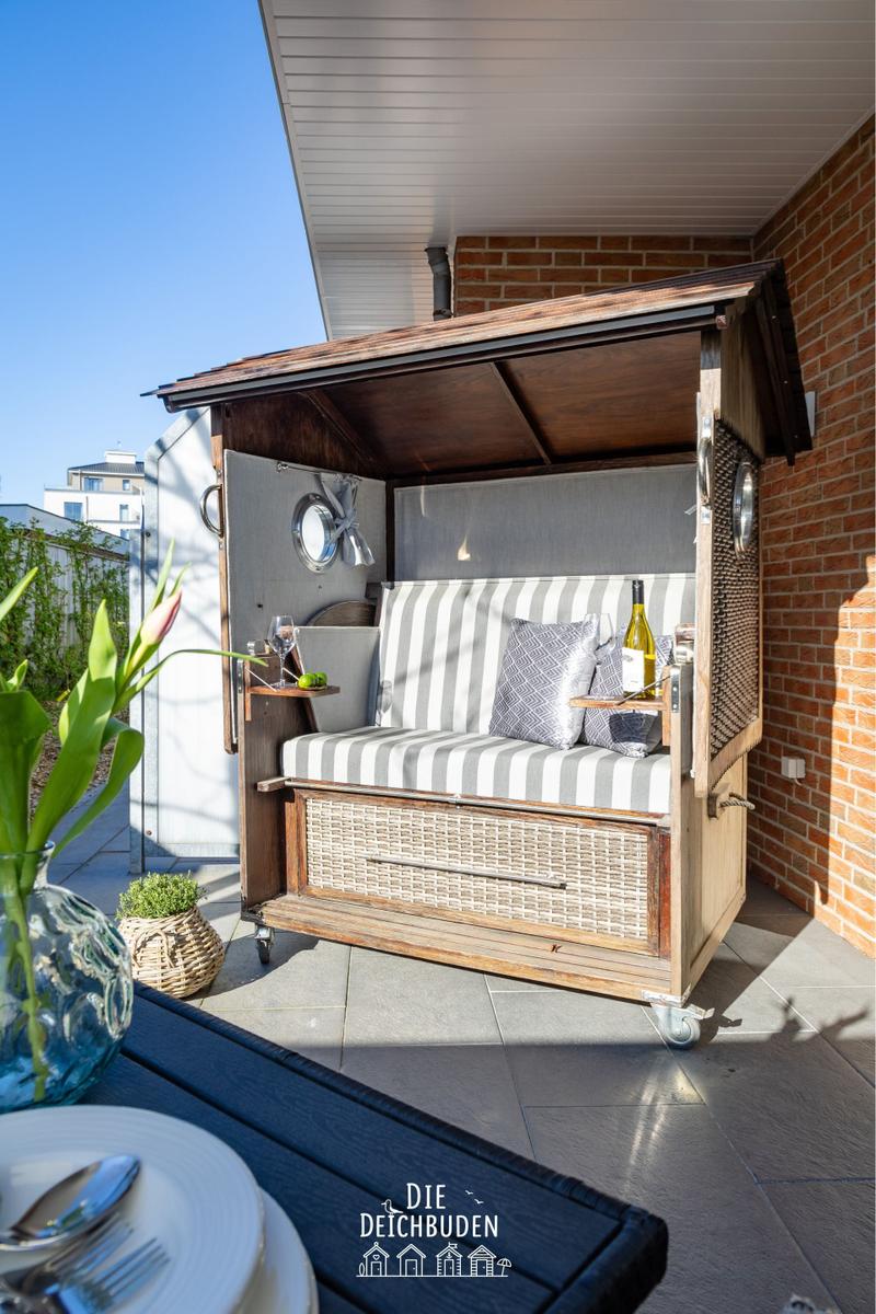 Holzschuppen mit Sitzbank, Kissen und Flasche auf Terrasse.