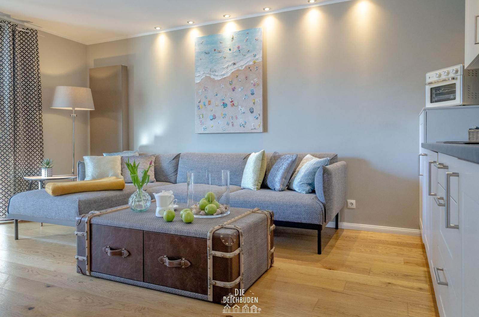 Wohnzimmer mit Sofa, Kaffeetisch und Küchenbereich. Wandbild und Holzboden.