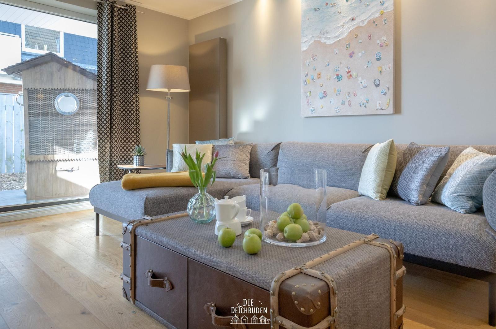 Ein Wohnzimmer mit grauem Sofa, Holzboden und einem Koffer als Couchtisch.