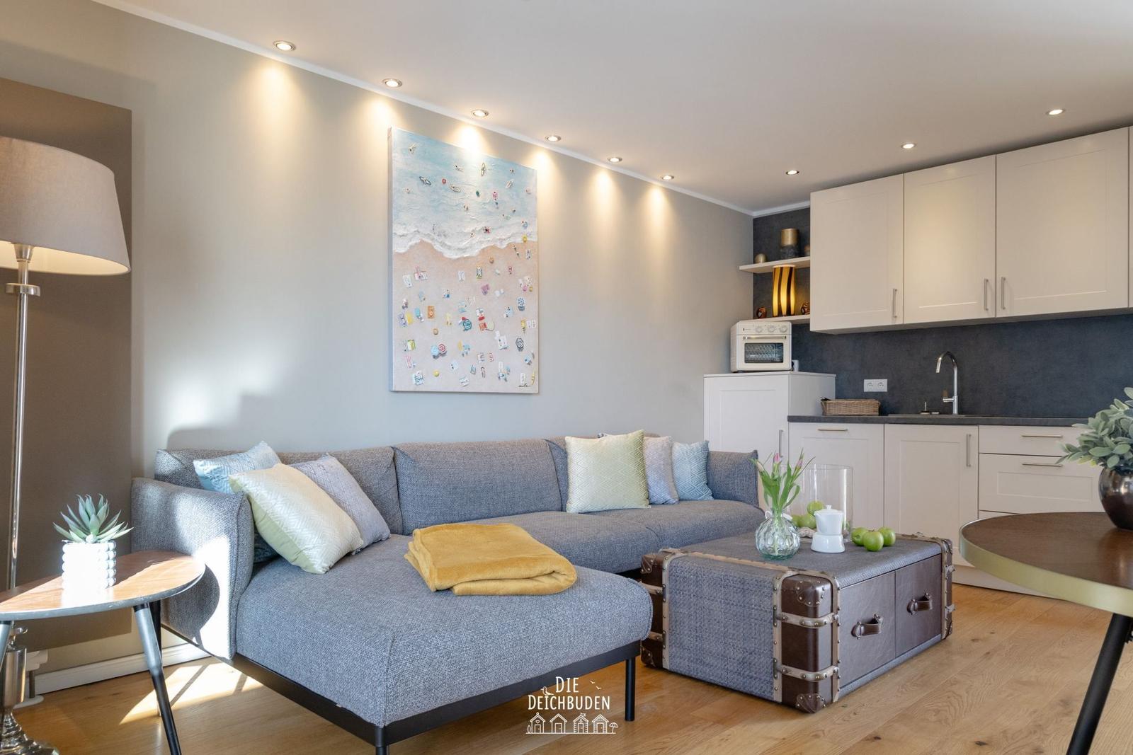 Wohnbereich mit Sofa, Kiste als Tisch und Küchenzeile.